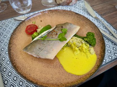 Sebzeli ve taze bitkilerle süslenmiş kremalı sarı soslu zarif Arktik Char Bifteği.