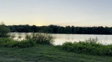 Sakin bir gölün üzerinde sakin bir gün batımı Yoğun ağaçlar ve bitki örtüsüyle çevrili, Altın Işık Sakin Su 'ya yansıyor