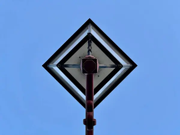Tek bir fener ile klasik bir sokak lambasının altından simetrik görüş, geometrik desenler ve açık mavi gökyüzüne karşı minimalist tasarım odaklı
