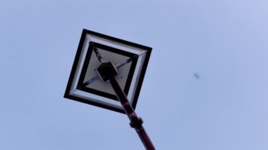 Klasik bir sokak lambasının yukarı doğru perspektifi açık mavi gökyüzünün tam altından görülen tek bir fener ile geometrik tasarım ve mimari basitliği vurguluyor.
