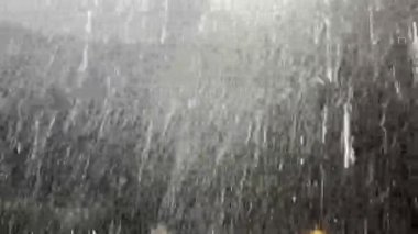 Şiddetli yağış, hafif ışık altında yoğun yağmur damlalarının düşmesiyle, dramatik ve atmosferik bir yağmur sahnesi yaratıyor.