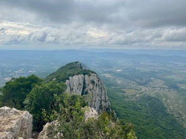 Pic Saint-Loup 'taki Engebeli Kireçtaşı Uçurumları ve Verdant Tepeleri' nin Uçsuz bucaksız Güney Fransa Ovaları Moody Skies altında