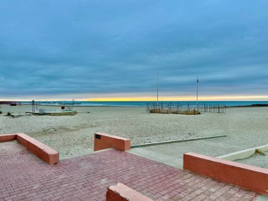 Deserted Mediterranean Beach at Sunrise with Cloudy Sky, Calm Waves, and Empty Structures on the Shoreline in Palavas-les-Flots, France clipart