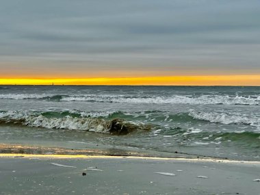 Golden Sunrise Over the Mediterranean Sea with Rolling Waves, Reflections on Wet Sand, and a Sailboat on the Horizon Near Palavas-les-Flots, France clipart