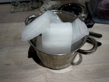 Close-Up of Ice Blocks in a Stainless Steel Pot on a Wooden Surface, Highlighting Chilled Storage or Cooling Concepts in a Domestic Setting clipart