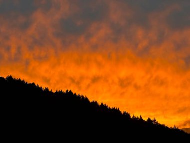 Alacakaranlıktaki Siluetli Dağ Sırtı 'nda Ateşli Portakal Bulutlarıyla dramatik Günbatımı Gökyüzü