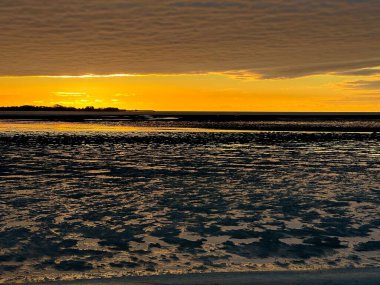 Vibrant Sunset Reflecting on the Bay of Somme Mudflats in October, Capturing the Golden Glow, Rippling Tidal Patterns, and a Dramatic Horizon from Le Crotoy clipart