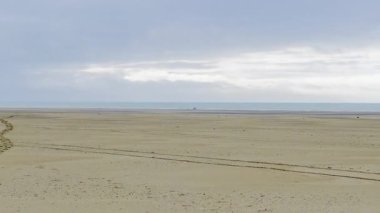 Geniş kumlu kıyı şeridi, sakin okyanus suları ve katmanlı bulutlarla dolu dramatik bir gökyüzü ile alçak gelgitte Authie Körfezi 'nin engin ve sakin manzarası barışçıl ve atmosferik bir kıyı manzarası yaratıyor.