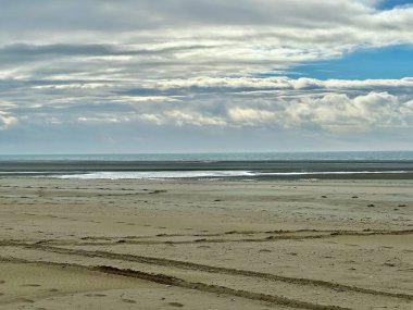 Vast and serene view of Authie Bay at low tide, with expansive sandy shoreline, calm ocean waters, and a dramatic sky filled with layered clouds, creating a peaceful and atmospheric coastal landscape clipart