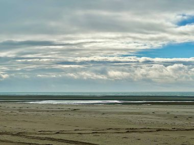 Geniş kumlu kıyı şeridi, sakin okyanus suları ve katmanlı bulutlarla dolu dramatik bir gökyüzü ile alçak gelgitte Authie Körfezi 'nin engin ve sakin manzarası barışçıl ve atmosferik bir kıyı manzarası yaratıyor.