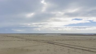 Geniş kumlu kıyı şeridi, sakin okyanus suları ve katmanlı bulutlarla dolu dramatik bir gökyüzü ile alçak gelgitte Authie Körfezi 'nin engin ve sakin manzarası barışçıl ve atmosferik bir kıyı manzarası yaratıyor.