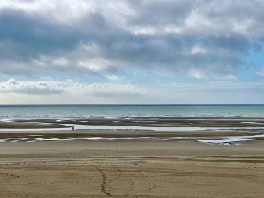 Uçsuz bucaksız ve sakin deniz manzarası kumsalları, gelgit havuzları ve kasvetli bir gökyüzünün altında kumdaki ayak izleri ve Authie Körfezi sahilini keşfeden yalnız figürlerle dolu uzak bir ufuk.