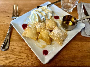 Bol yağda kızartılmış, balla sulandırılmış, pudra şekerli, kremalı, kırmızı meyve soslu ve küçük metal bir bardak ekstra şuruplu gurme tatlı tabağı.