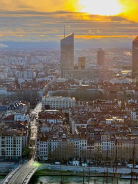 Lyon, Fransa - 23 Mart 2025: Modern gökdelenlerin ve tarihi çatıların siluetleri ile Lyon şehrinin üzerinde geniş panoramik gündoğumu manzarası, bulutlarla dolu bir gökyüzünün altında Fourviere tepesinden görüldü.
