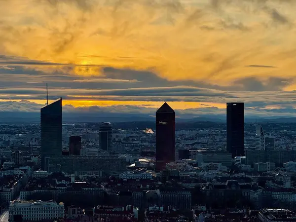 Lyon, Fransa - 23 Mart 2025: Modern gökdelenlerin ve tarihi çatıların siluetleri ile Lyon şehrinin üzerinde geniş panoramik gündoğumu manzarası, bulutlarla dolu bir gökyüzünün altında Fourviere tepesinden görüldü.