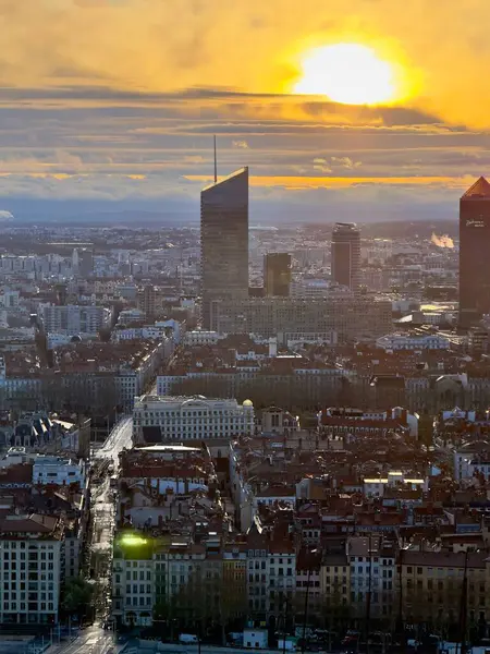 Lyon, Fransa - 23 Mart 2025: Modern gökdelenlerin ve tarihi çatıların siluetleri ile Lyon şehrinin üzerinde geniş panoramik gündoğumu manzarası, bulutlarla dolu bir gökyüzünün altında Fourviere tepesinden görüldü.