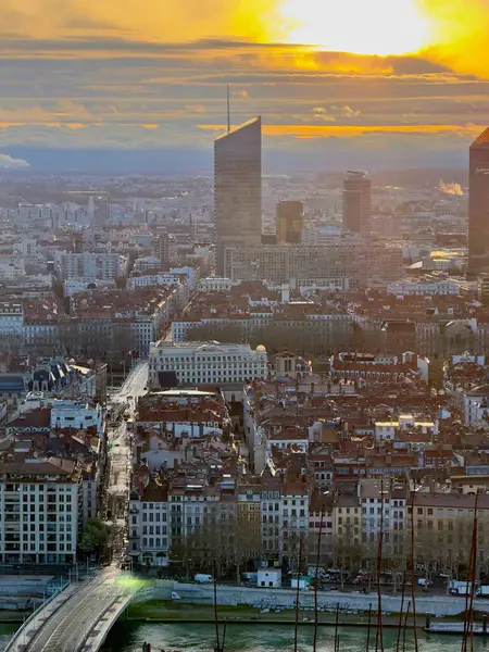 Lyon, Fransa - 23 Mart 2025: Modern gökdelenlerin ve tarihi çatıların siluetleri ile Lyon şehrinin üzerinde geniş panoramik gündoğumu manzarası, bulutlarla dolu bir gökyüzünün altında Fourviere tepesinden görüldü.