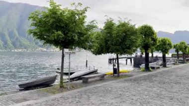 Lenno, İtalya - 2 Mayıs 2025: Lenno ve Ossuccio 'daki huzurlu göl gezintisi, düzgün budanmış ağaçlar, sahil bankları, dağ manzaraları, renkli köyler ve Como Gölü üzerindeki manzaralı perspektifler