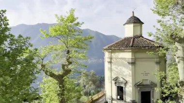 Sabahın erken saatlerinde Como Gölü ve etrafındaki dağların Sacro Monte di Ossuccio, İtalya 'daki hac yolundan zeytin ağaçları, çatılar ve bulutları delen yumuşak güneş ışınlarıyla manzarası.