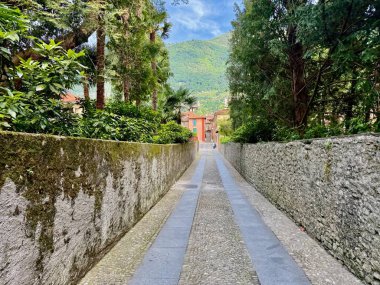 Via alla Torre yolu yosun kaplı taş duvarlar ve yemyeşil Akdeniz yeşili arasında uzanan dar kaldırımlar yemyeşil Prealpine tepeleri, Lenno, Como Gölü, İtalya