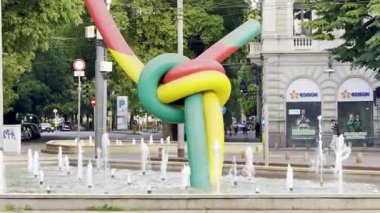 Milan, İtalya - 4 Mayıs 2025: Milano, İtalya 'da renkli çağdaş heykel, kentsel arka plandaki çeşmeden yükselerek, Cadorna istasyonu yakınlarındaki moda ve tasarımı sembolize ediyor