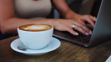 Tanınmayan bir kadın bir fincan kahveyle kafede oturuyor ve dizüstü bilgisayarda çalışıyor. Yüksek kalite 4k görüntü