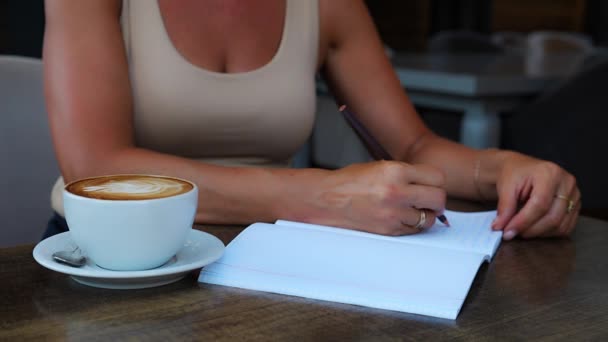 認識できない女性がコーヒーを飲みながらカフェのテーブルに座り ノートに書き込み情報を書き込みます 高品質4K映像 — ストック動画