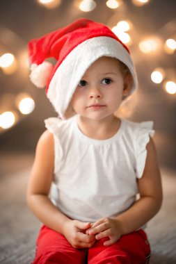 Kırmızı şapkalı ve beyaz gömlekli şirin küçük bir kız. Küçük bir çocuk ve arka planda çelenk olan bir Noel konsepti. Yüksek kalite fotoğraf