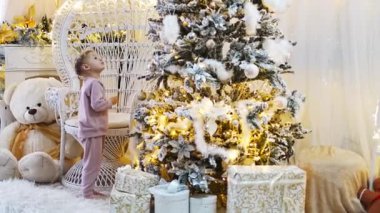 Evin parlak iç kısımlarında, Noel ağaçlarının yanında pijamalı, sevimli küçük bir kız. Yüksek kalite 4k görüntü