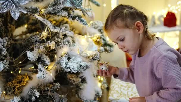 家の明るいインテリアのクリスマスツリーの近くのパジャマで非常に素敵なチャーミングな女の子のブロンド 高品質4K映像 — ストック動画