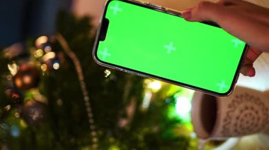 Yakın plan çekimde, Noel ve Yeni Yıl süresince yeşil Noel ağacı süslemeleri üzerinde renkli toplar bulunan akıllı telefonlar kullanılıyor. Yüksek kalite 4k görüntü
