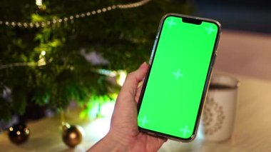 Yakın plan çekimde, Noel ve Yeni Yıl süresince yeşil Noel ağacı süslemeleri üzerinde renkli toplar bulunan akıllı telefonlar kullanılıyor. Yüksek kalite 4k görüntü