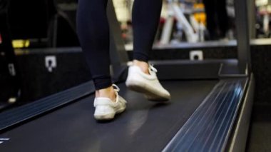 Genç bir kadın spor salonunda koşu bandına çıkıyor. Yürüyerek yaklaş. Yüksek kalite 4k görüntü