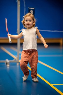 Little girl three years old playing badminton in sport wear on indoor court . High quality photo