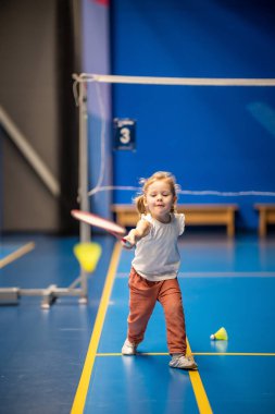 Little girl three years old playing badminton in sport wear on indoor court . High quality photo