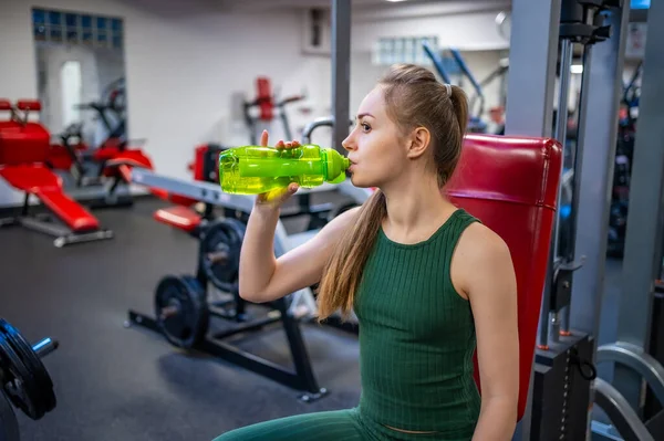 Spor eğitiminden sonra mola veren ve yeşil cam şişeden su içen genç bir kadın. Kişisel bakım, yaşam dengesi ve sağlıklı yaşam tarzı konsepti. Yüksek kalite fotoğraf