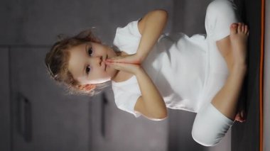 Little cute girl in a lotus pose practicing yoga and breathing practices on grey background in dark room. High quality 4k footage