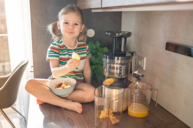 Little girl making fresh juice sitting on the table in home kitchen. High quality photo