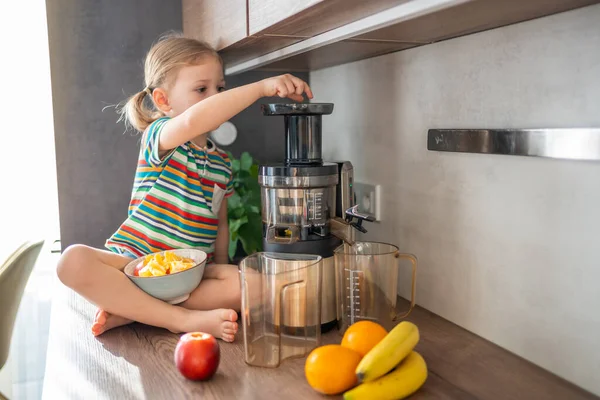 Little girl making fresh juice sitting on the table in home kitchen. High quality photo