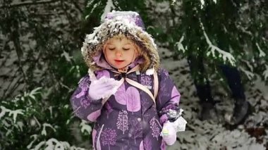 Kar deneyen küçük bir kız, ağır çekimde. Mutlu çocuk kışın kar ağacı arka planında sevinir. Çocuk Prag parkında karla oynuyor. Yüksek kaliteli FullHD görüntüler