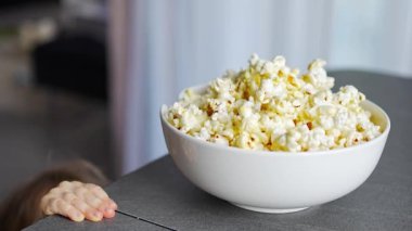 Little girl is eating popcorn in home kitchen. Focus on hand taking popcorn. High quality 4k footage