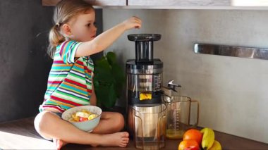 Little girl making fresh juice sitting on the table in home kitchen. High quality 4k footage