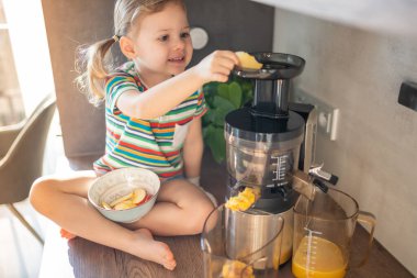 Little girl making fresh juice sitting on the table in home kitchen. High quality photo