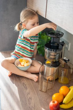 Little girl making fresh juice sitting on the table in home kitchen. High quality photo