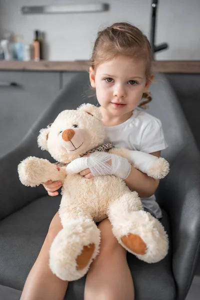 Little girl with broken finger holds teddy bear with a bandaged paw at the doctor\'s appointment in the hospital. High quality photo