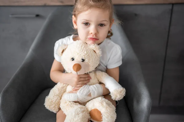 Little girl with broken finger holds teddy bear with a bandaged paw at the doctor\'s appointment in the hospital. High quality photo