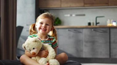 Cute little girl hugging teddy bear while sitting on sofa at home. High quality 4k footage