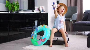 Little girl on suitcase baggage luggage and inflatable life buoy playing with toy plane and ready to go for traveling on vacation. High quality 4k footage