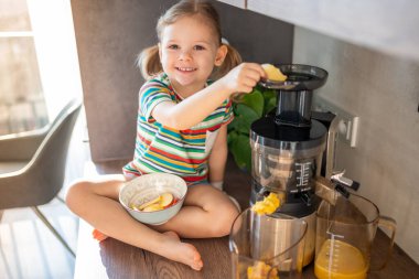 Little girl making fresh juice sitting on the table in home kitchen. High quality photo