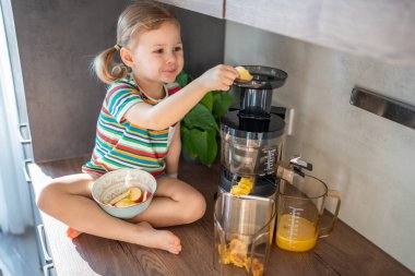 Little girl making fresh juice sitting on the table in home kitchen. High quality photo